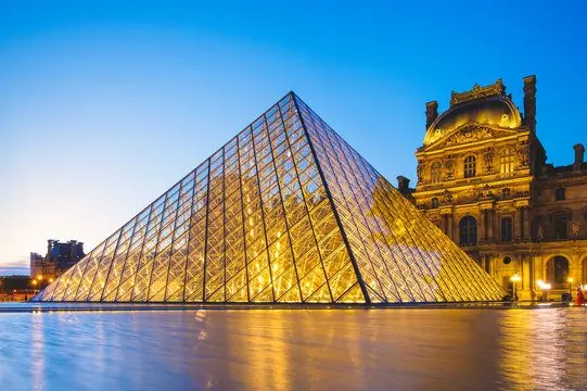 The Louvre pyramid lit up at dusk in front of the palace façade, Paris